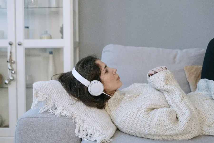 Woman lying on a sofa, wearing headphones, relaxed and cozy indoors, capturing a moment of tranquility.